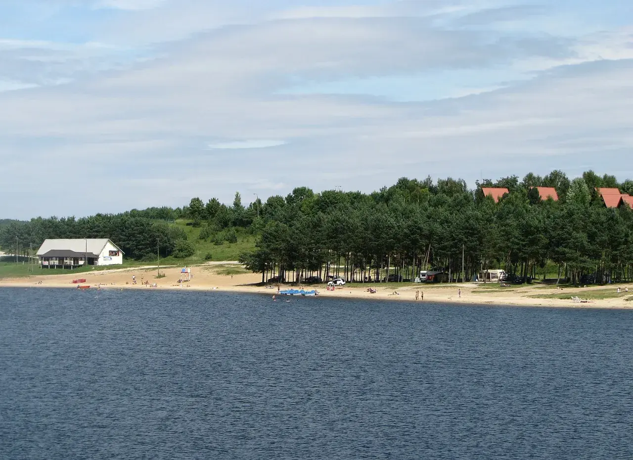 Słoneczny dzień nad zalewem Chańcza. Plaża z ludźmi, domki letniskowe i las.