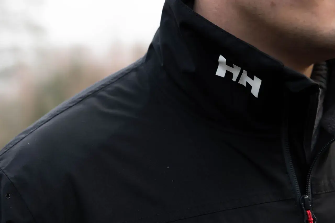 Czarna kurtka z białym logo HH. Helly Hansen to firma znana z odzieży outdoorowej i żeglarskiej.