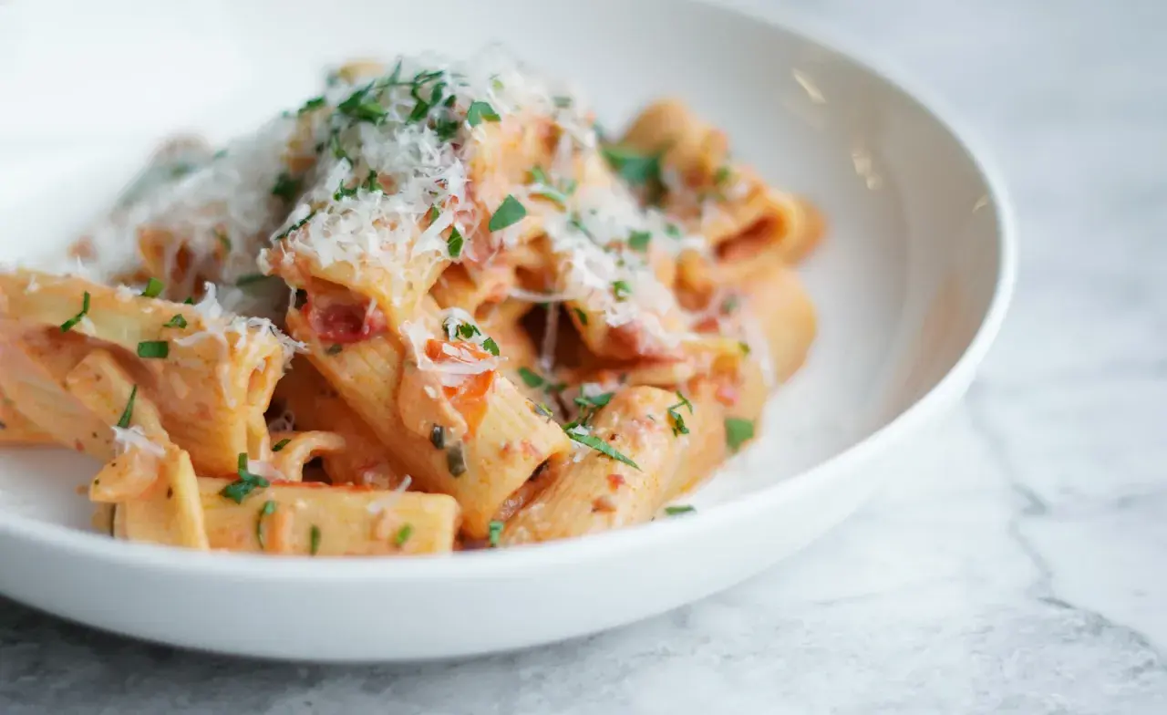 Pyszne rigatoni w kremowym sosie pomidorowym, posypane parmezanem i natką pietruszki. Idealny przepis na szybki obiad.