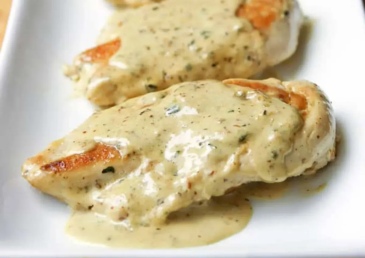 Deux morceaux de poulet à la crème, nappés d'une sauce onctueuse aux herbes, sur une assiette blanche.