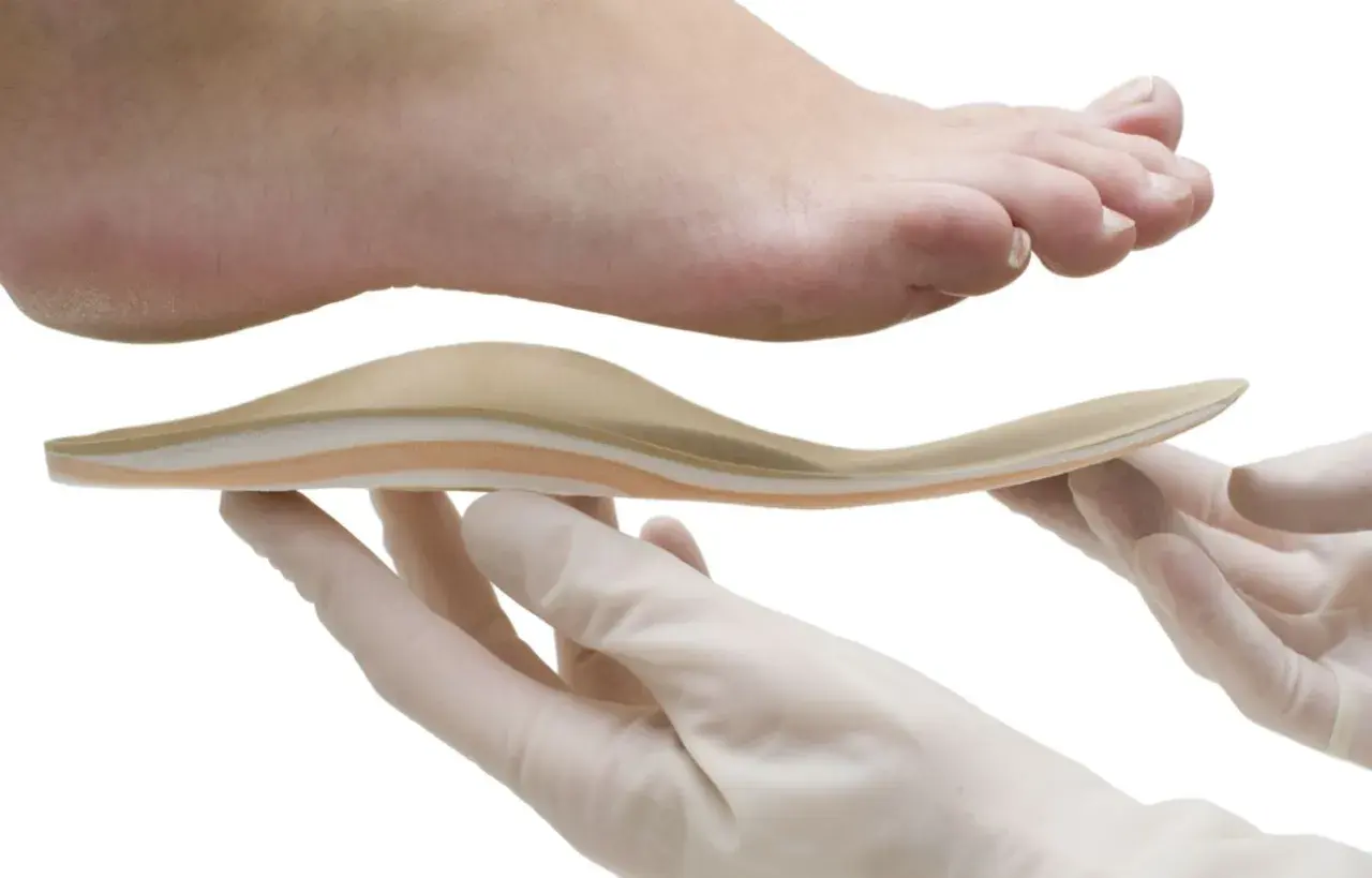 Fuß mit Plattfuß wird mit einer Einlage behandelt. Hände in Handschuhen halten die orthopädische Einlage.