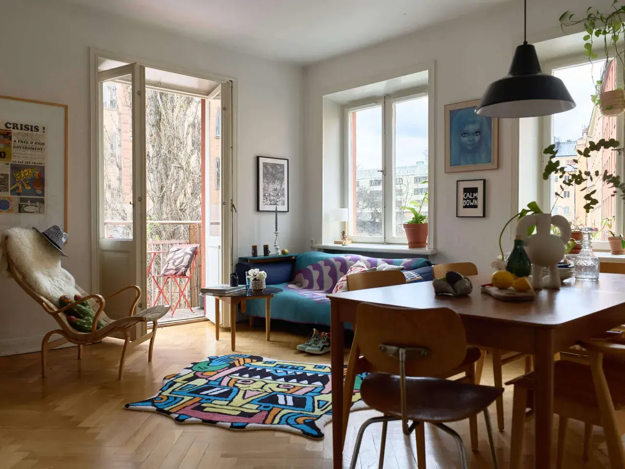 En ljus och färgstark lägenhet med 60-tals inredning. En blå soffa med mönstrat överkast, en trästol med fårskinn och en lekfull matta på parkettgolvet.