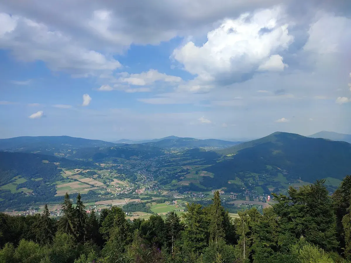 Widok z **szczebel szczyt** na dolinę z polami i lasami. Chmury na błękitnym niebie.