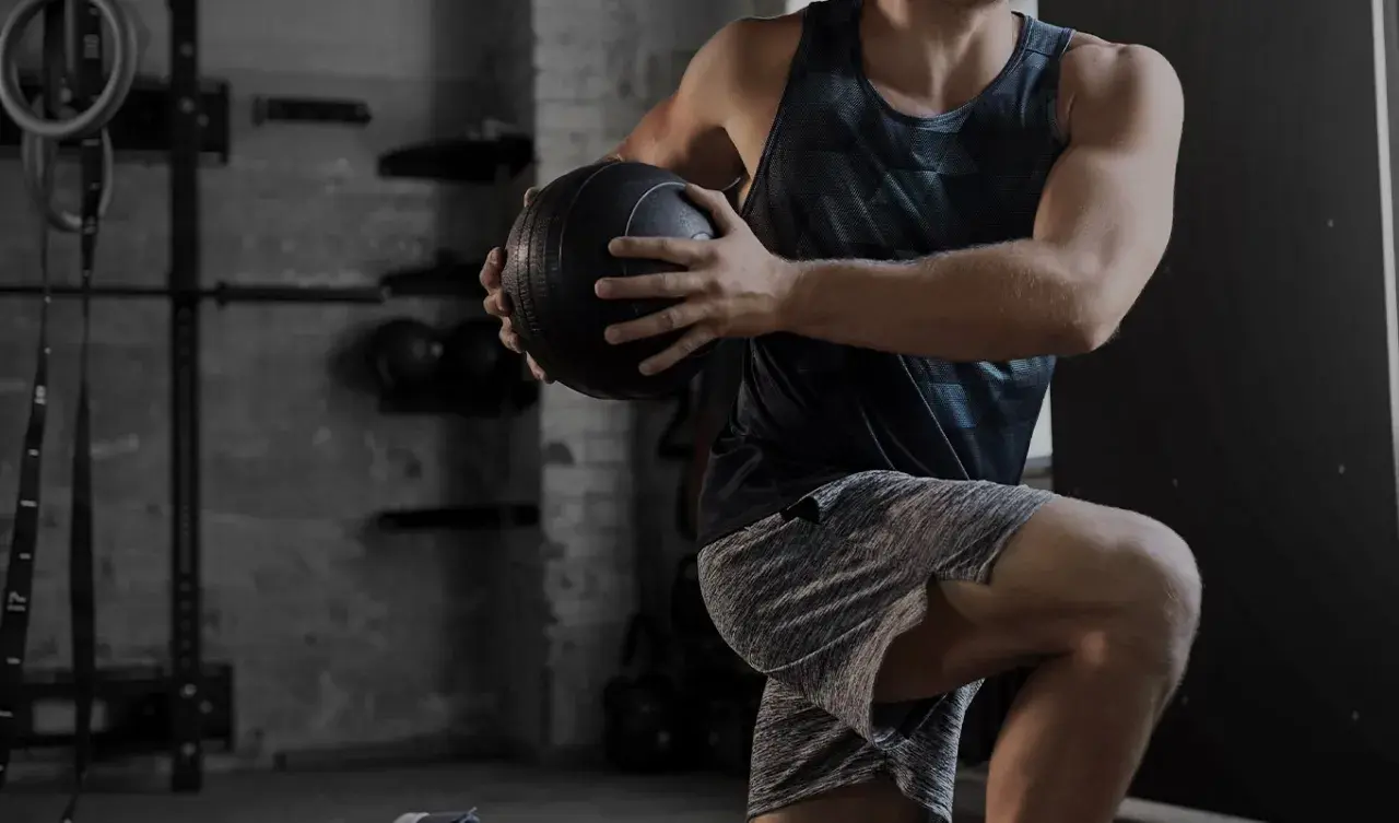 Uomo in palestra esegue un esercizio con palla medica. Gli aminoacidi essenziali a cosa servono? Aiutano la costruzione muscolare.