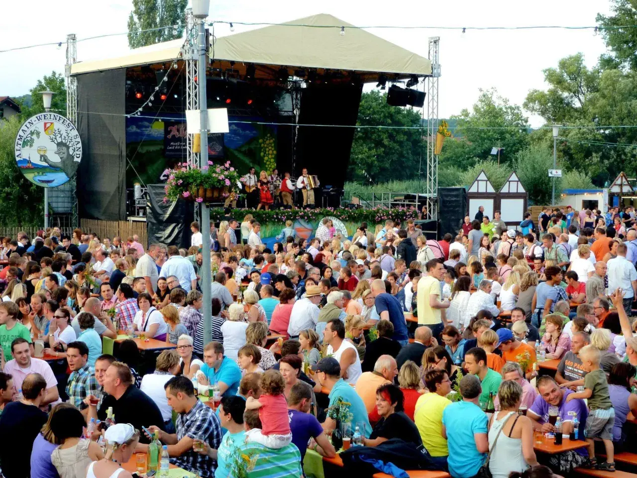Menschen feiern beim Weinfest Sand am Main. Eine Band spielt auf der Bühne, während Gäste an Tischen sitzen und die Atmosphäre genießen.
