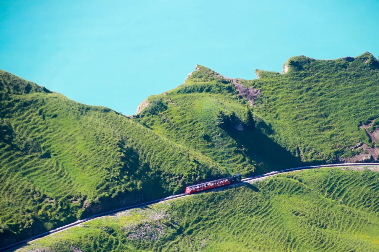 Rött tåg med passagerare på en bergssluttning vid en turkos sjö, en dröm för alla som älskar tåg interrail.