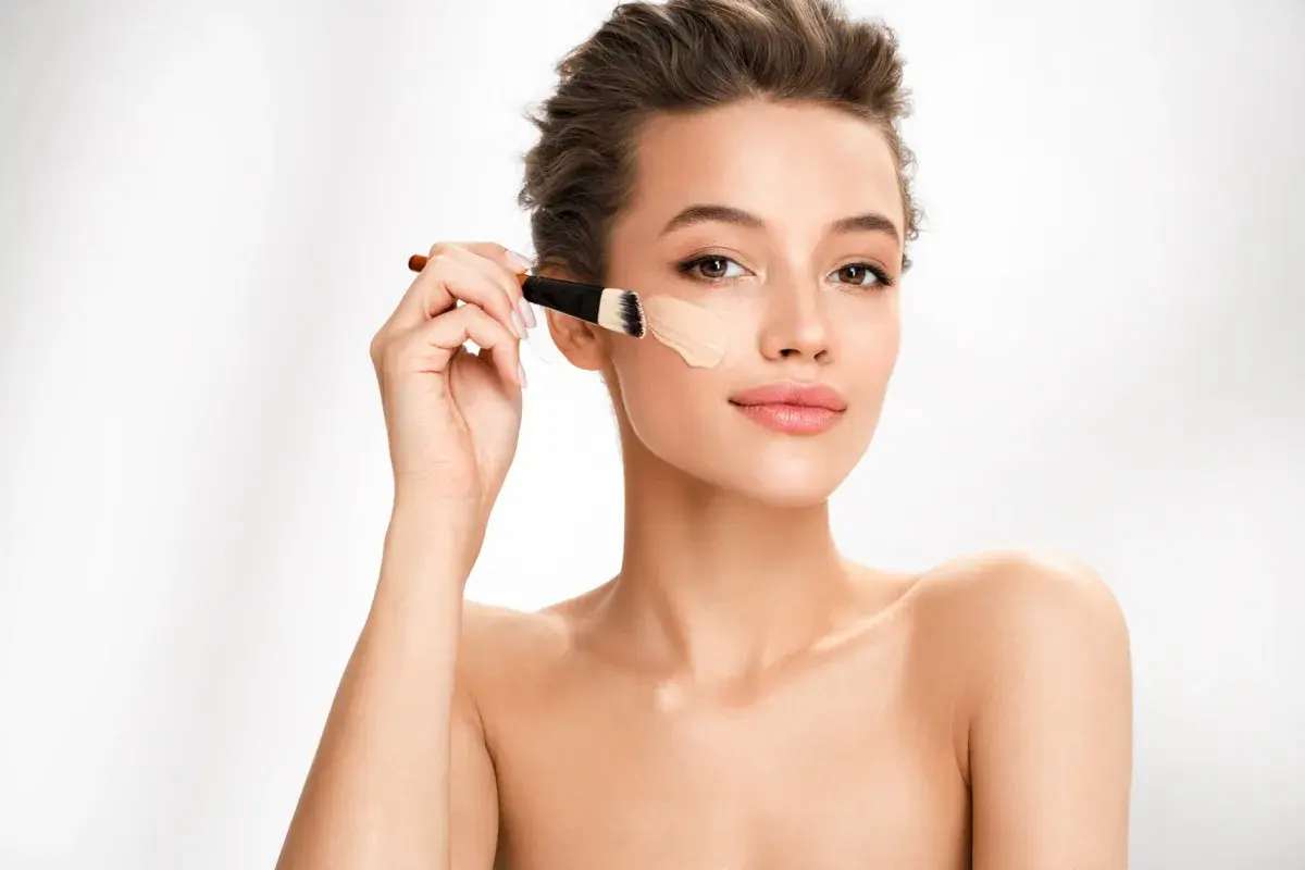 Donna applica il colore correttore con un pennello sul viso, creando una base perfetta.