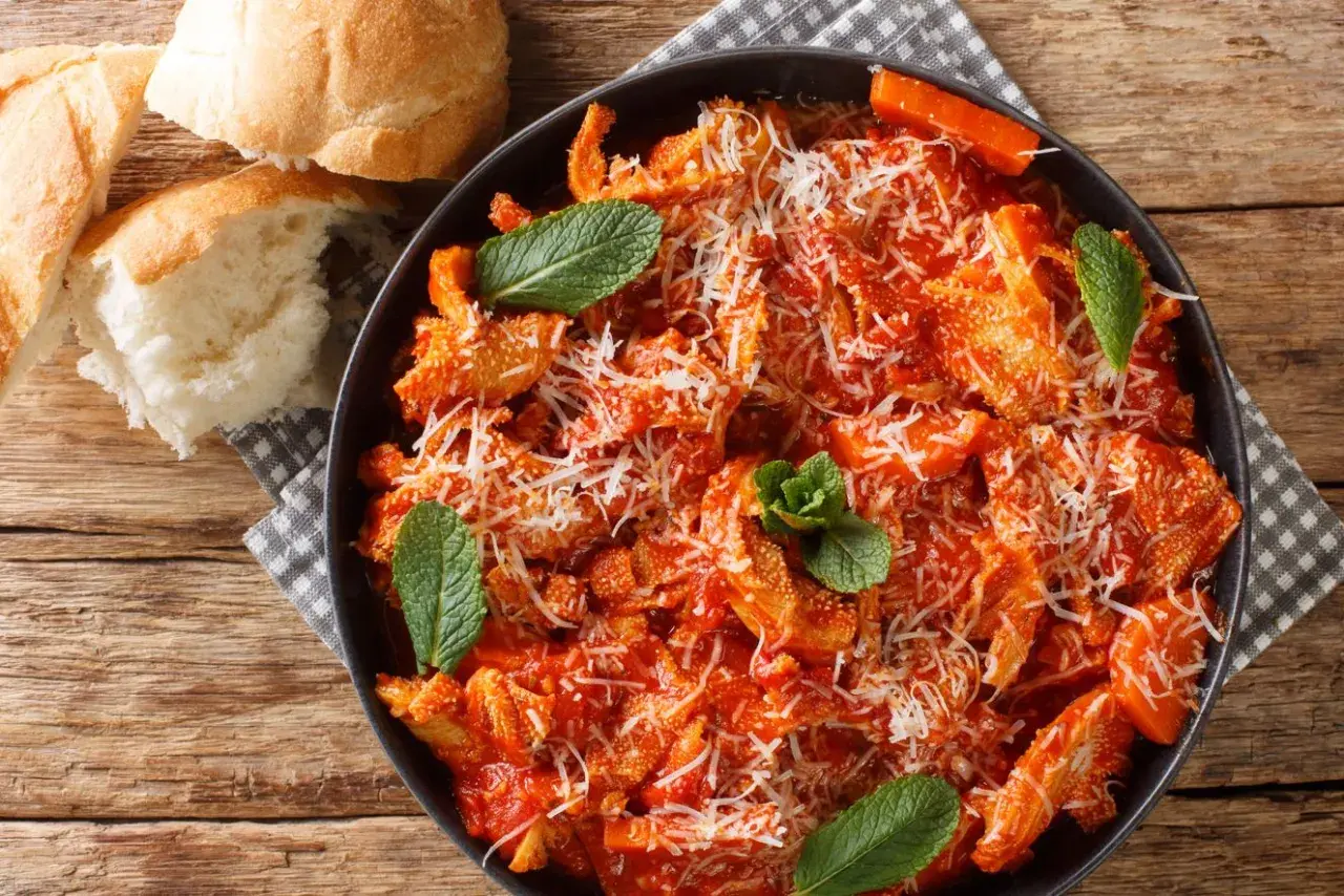Pyszne flaki po rzymsku w sosie pomidorowym, posypane parmezanem i udekorowane miętą. Obok świeże pieczywo.