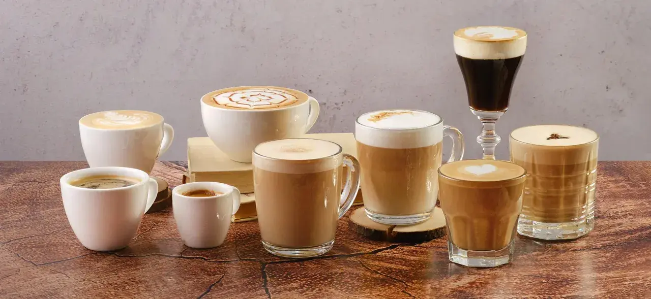 Vielfalt an Kaffee Kreationen: Latte Art, Espresso und cremige Cappuccinos in verschiedenen Tassen und Gläsern.