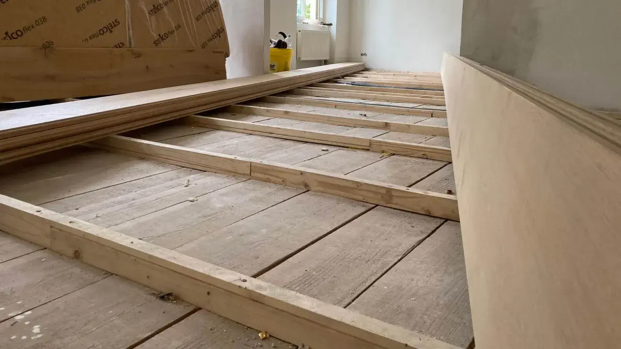 Holzbalken werden auf einem alten Holzboden verlegt, um ihn für neue Bodenplatten vorzubereiten. So kann man den Boden ausgleichen ohne Ausgleichsmasse.