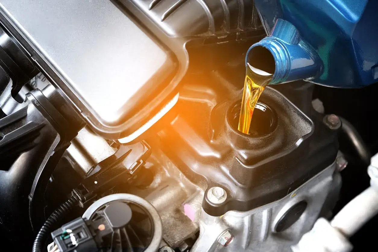 Vertiendo aceite de coche para moto en el motor. El líquido dorado fluye desde un envase azul hacia la abertura de llenado.
