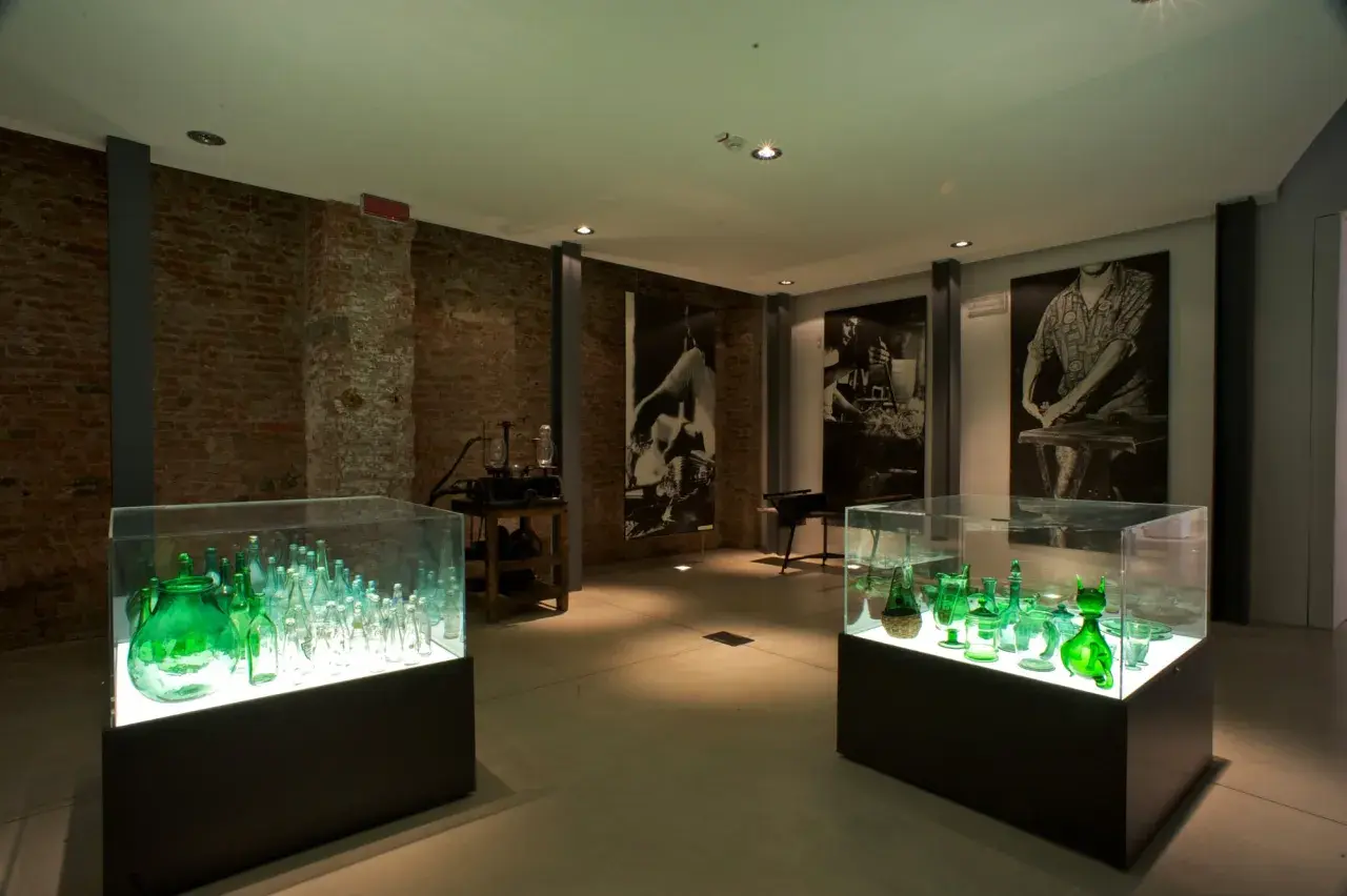 Vetrina con bottiglie verdi illuminate, un'esposizione che racconta cosa vedere a Empoli, tra storia e arte del vetro.