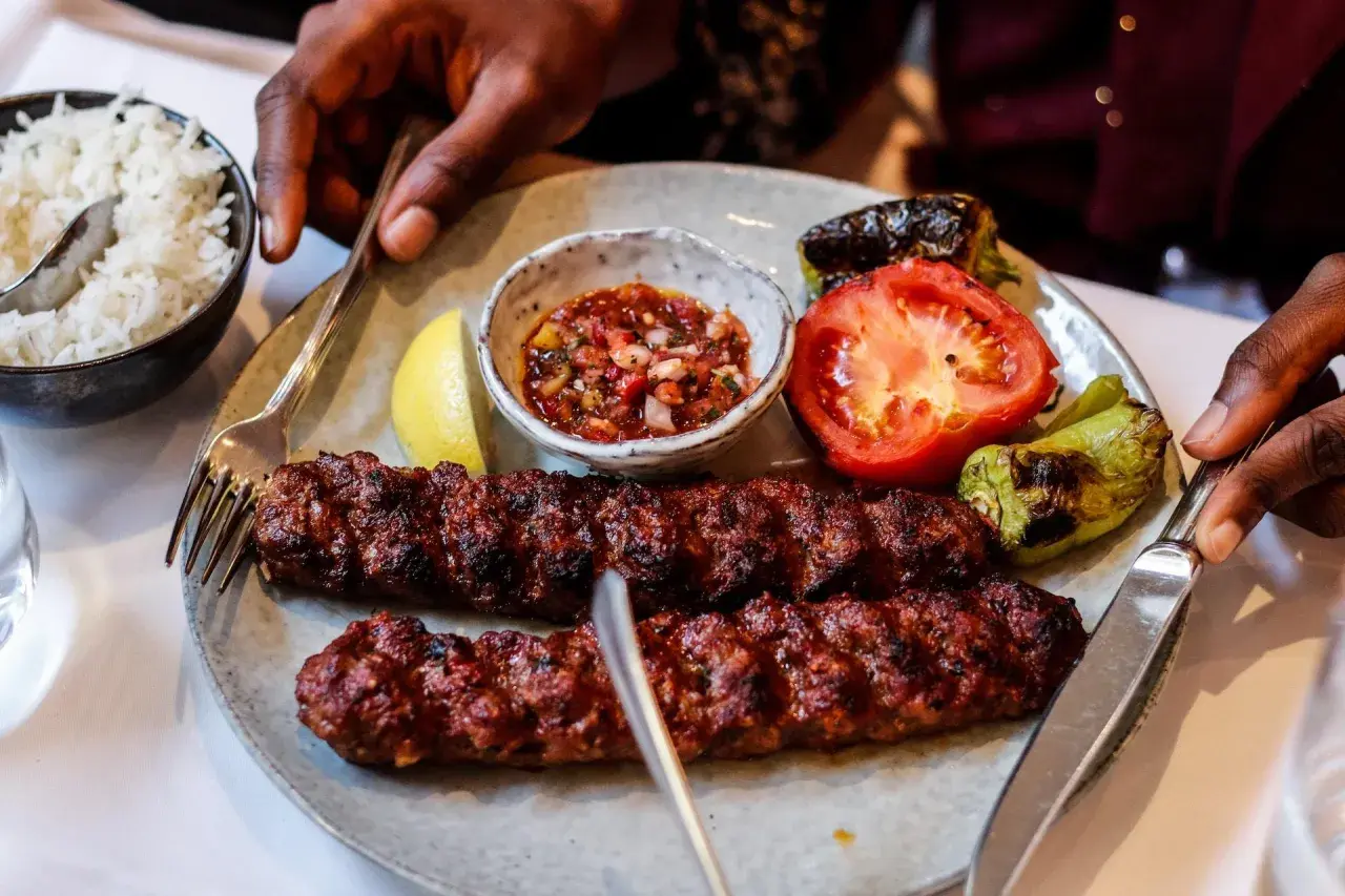 Dwa soczyste, grillowane kebaby na talerzu z ryżem, pomidorem, papryką i sosem. Tak wygląda pyszny kebab!