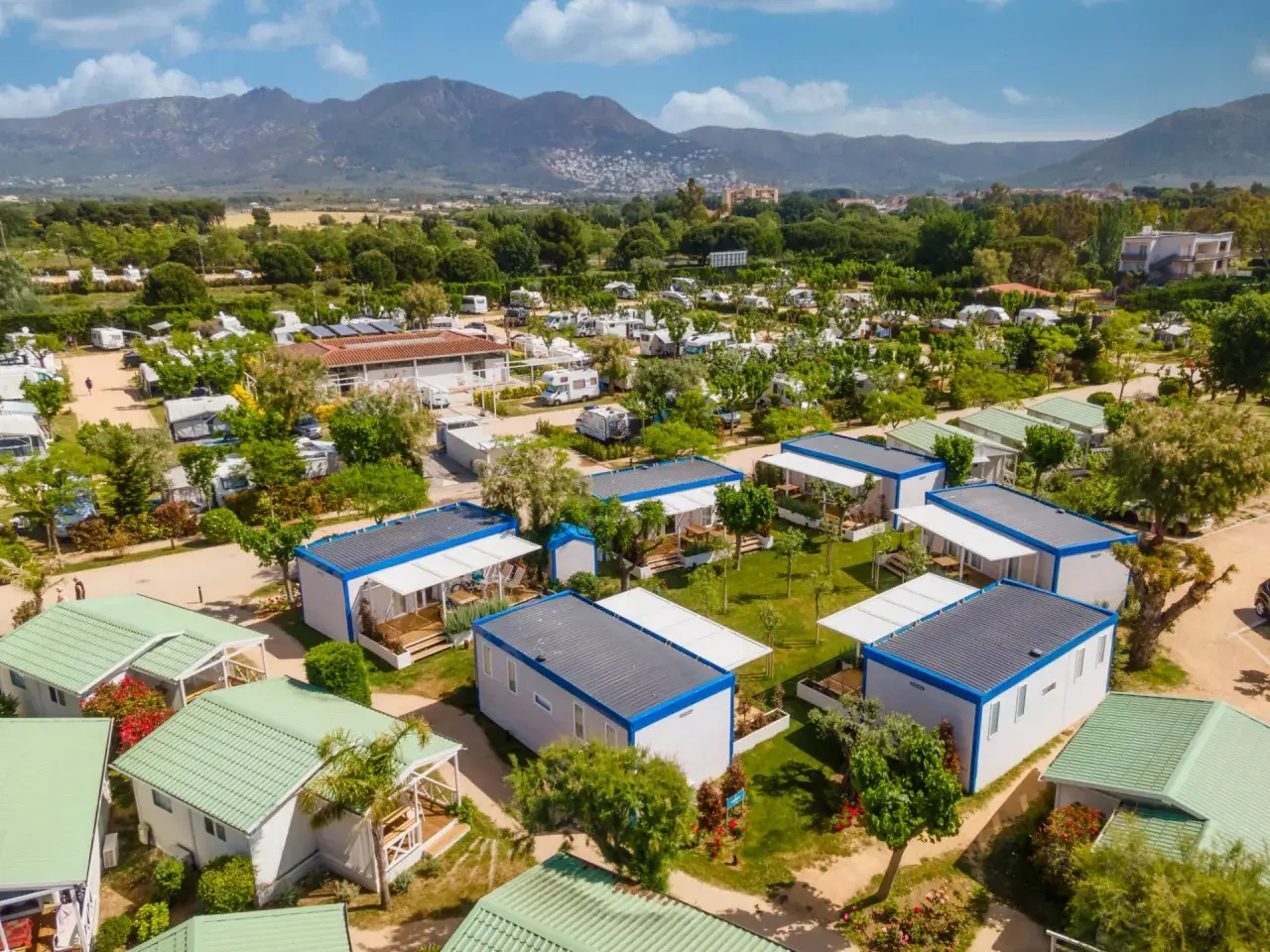 Un complejo de bungalows y caravanas para ir de camping, con montañas al fondo y un cielo azul.