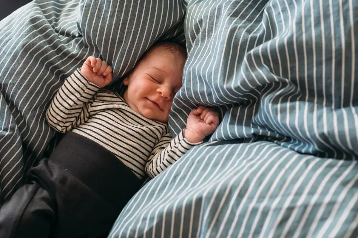En 5 månaders bebis sover sött i ett randigt täcke. Kanske drömmer hen om att slippa vakna ofta på natten.