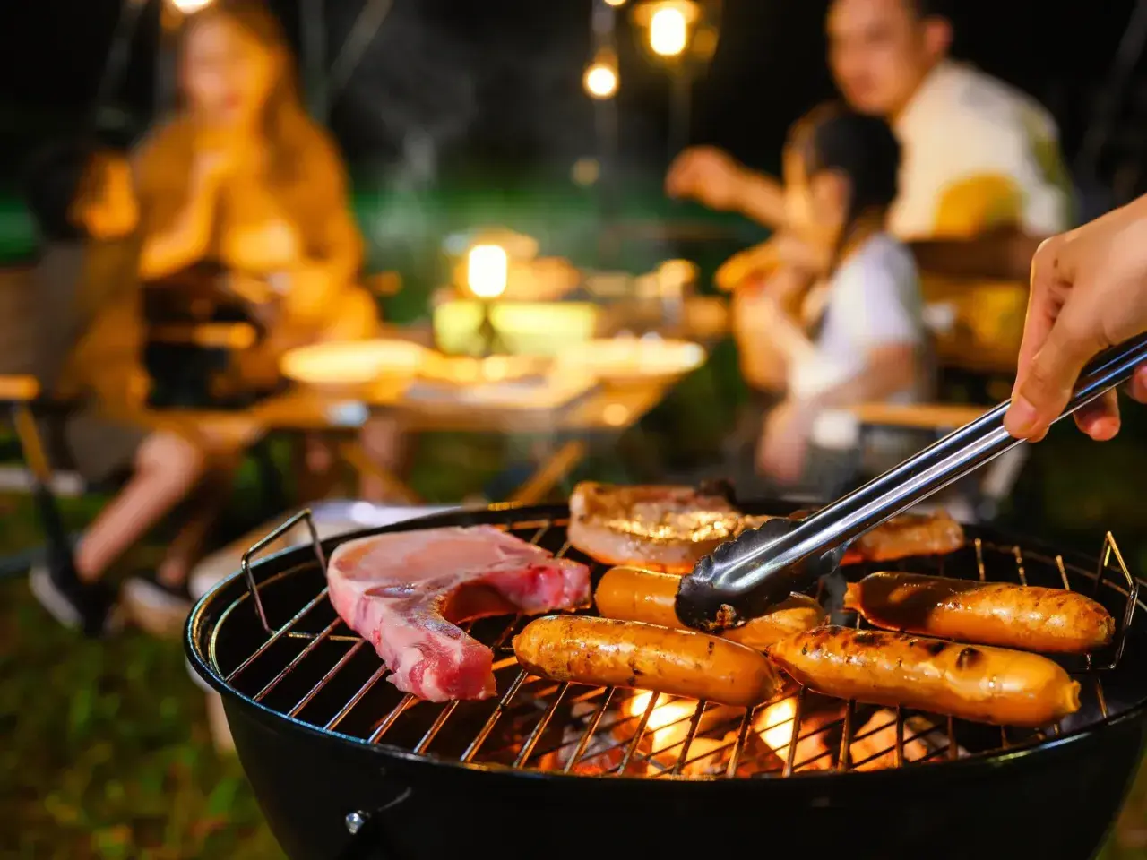 Une famille profite d'un barbecue en soirée. Des saucisses et une côte de porc cuisent sur le gril, la température de cuisson saucisse barbecue est parfaite.
