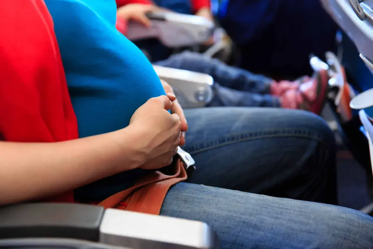 Gravid kvinna med magen i fokus, bekvämt sittande på ett flygplan. Hon håller handen över magen, redo att flyga gravid.