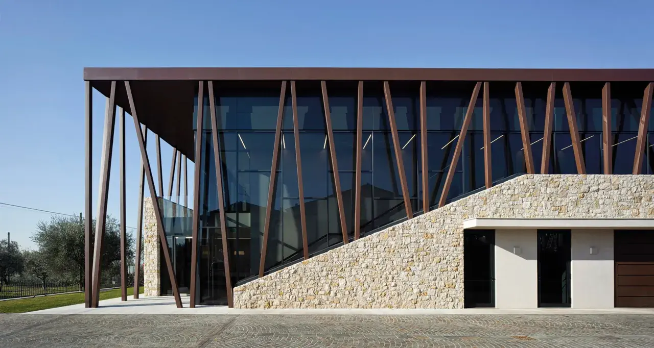 Edificio moderno con facciata in pietra e vetro, travi inclinate in metallo marrone. Un'architettura che evoca i valetti di Bardolino.