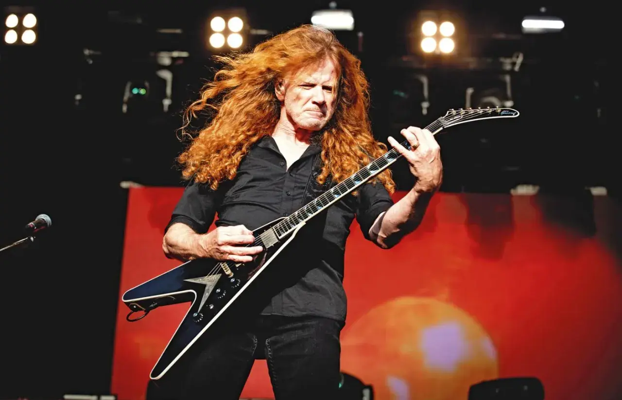 Dave Mustaine z burzą rudych włosów gra na gitarze w kształcie skrzydła.