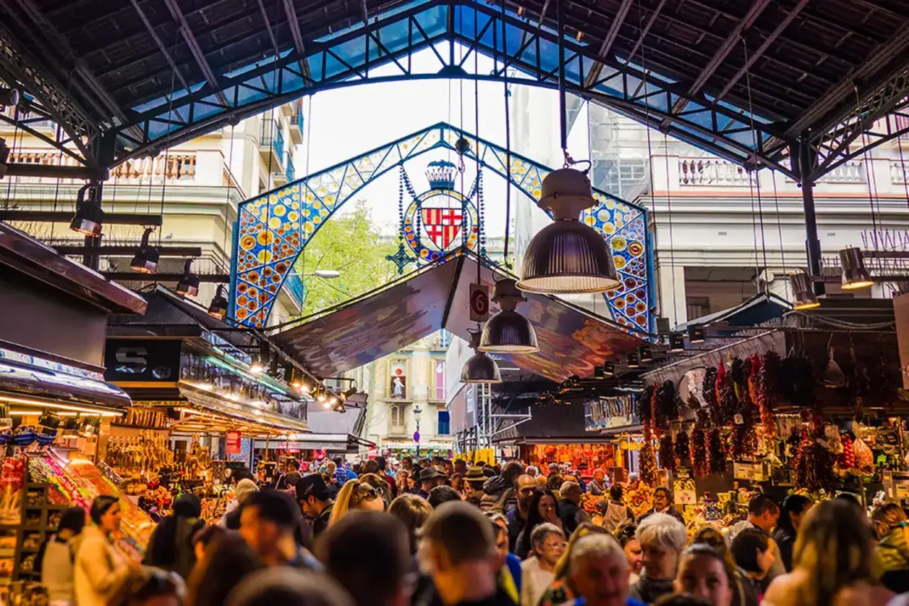 Tętniący życiem Mercat de la Boqueria w Barcelonie, pełen ludzi, kolorowych stoisk z jedzeniem i charakterystycznego, ozdobnego łuku.