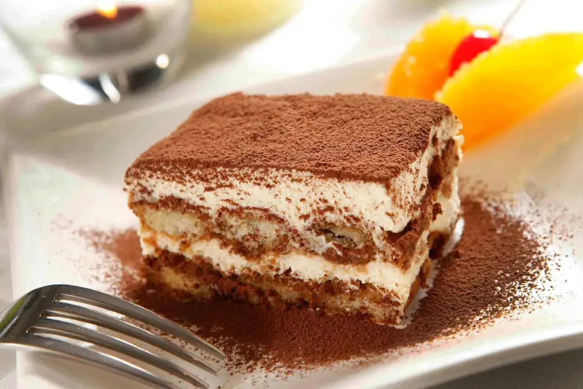Un délicieux tiramisu Kinder Bueno, saupoudré de cacao, avec des fruits en arrière-plan.