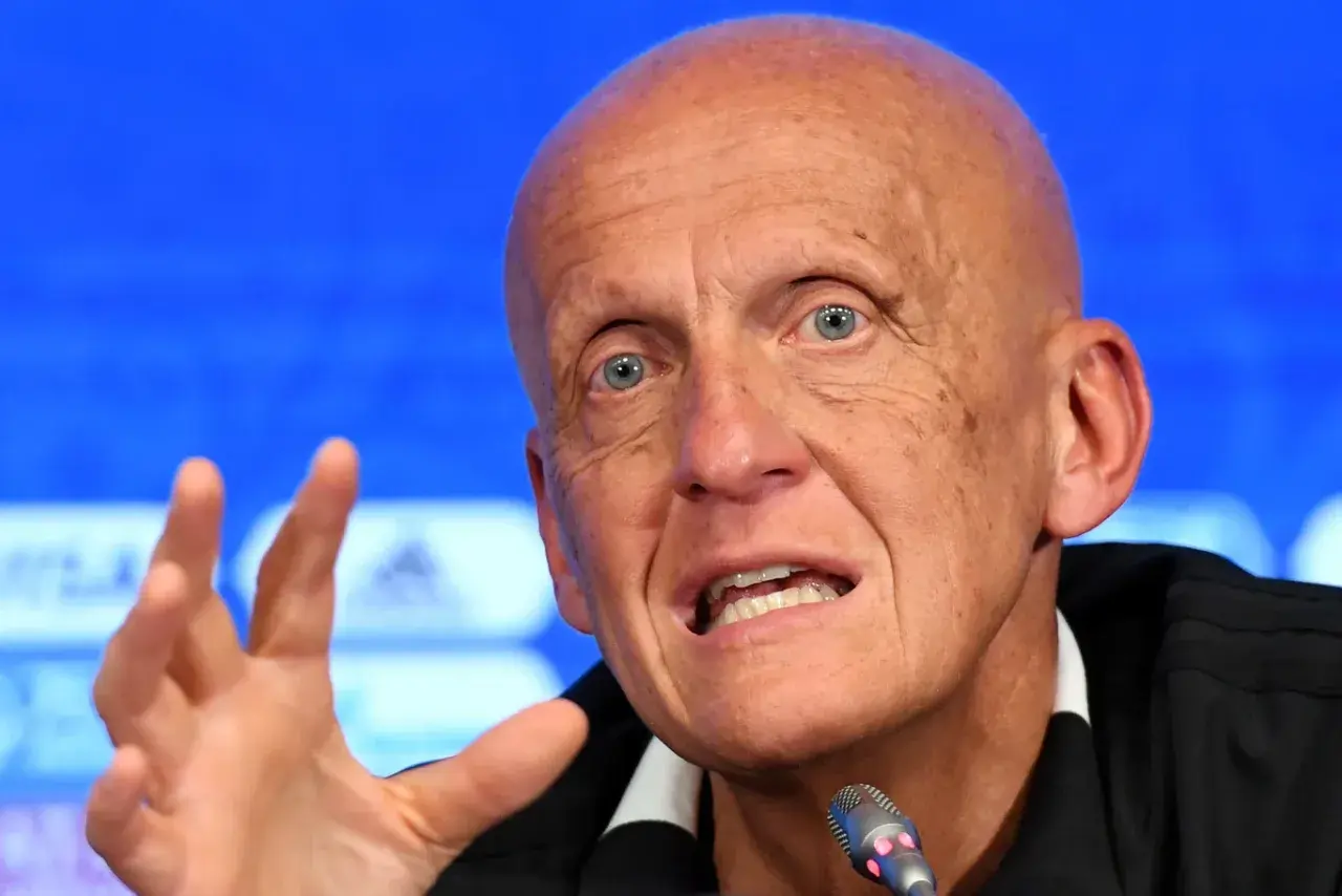 Pier Luigi Collina, znany sędzia piłkarski, przemawia do mikrofonu, gestykulując prawą ręką.