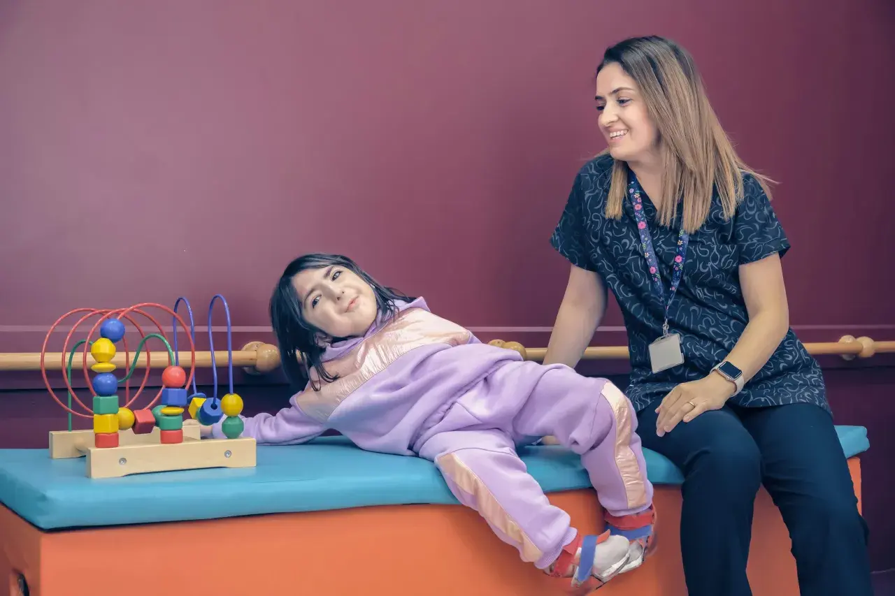 Uśmiechnięta terapeutka patrzy na dziecko bawiące się zabawką terapeutyczną.