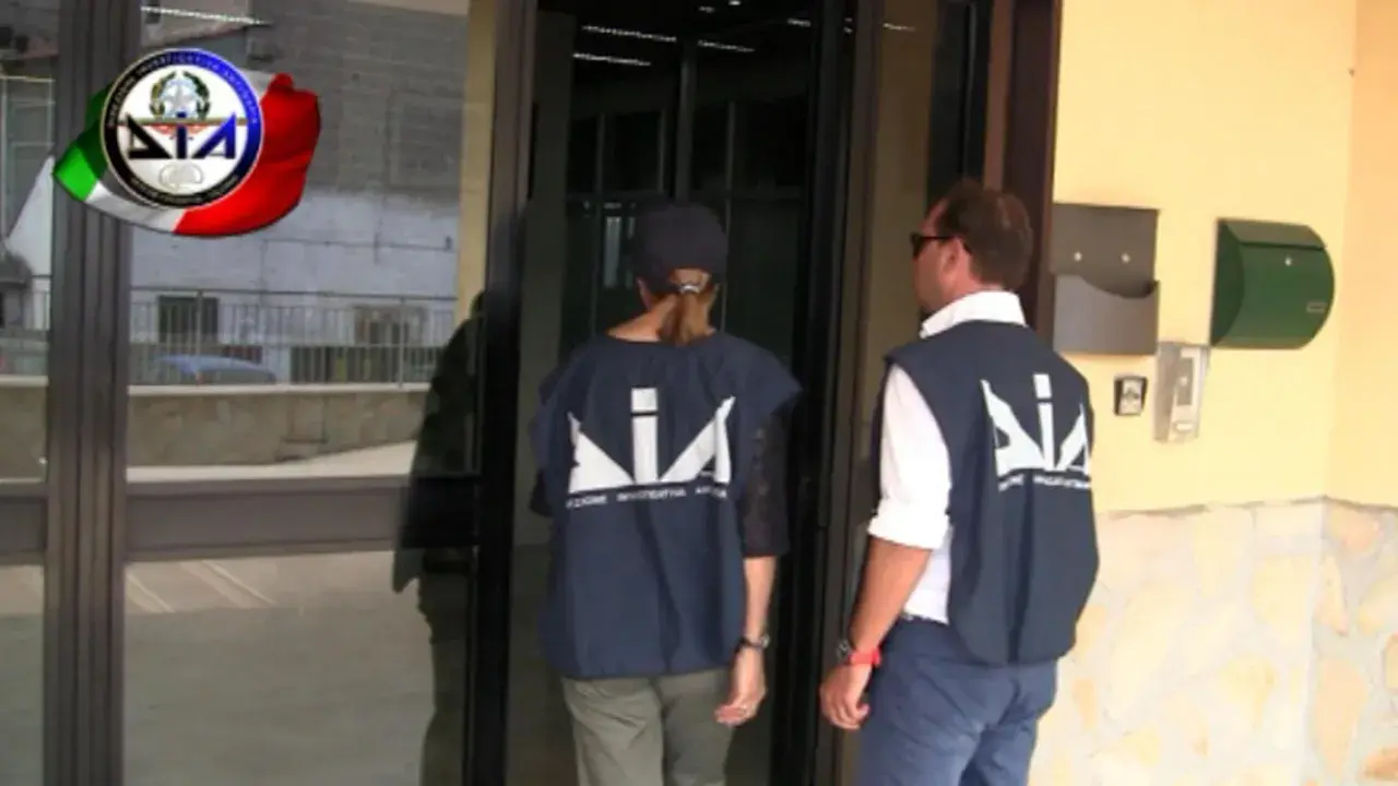 Agenti della DIA, Direzione Investigativa Antimafia, si avvicinano a un ingresso.
