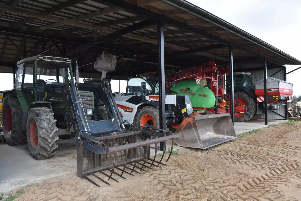 Ciągniki i maszyny rolnicze pod zadaszeniem. Widać zielony Fendt z ładowaczem, biały Bobcat, zielony opryskiwacz i ciągnik z rozsiewaczem. To wszystko w budynku gospodarczym bez zgłoszenia.