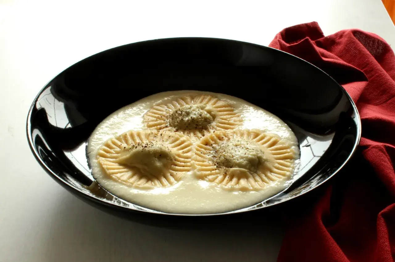 Tre ravioli di borragine, con un ripieno cremoso e una spolverata di pepe, serviti in una ciotola nera su un tovagliolo rosso.