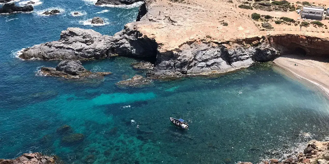 La cala Medina en Cabo de Palos, con aguas cristalinas y una pequeña embarcación, invita a explorar sus secretos.