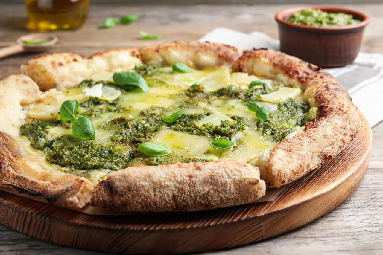 Pizza rustique au pesto, garnie de fines tranches de pommes de terre et de fromage fondant, décorée de feuilles de basilic frais.