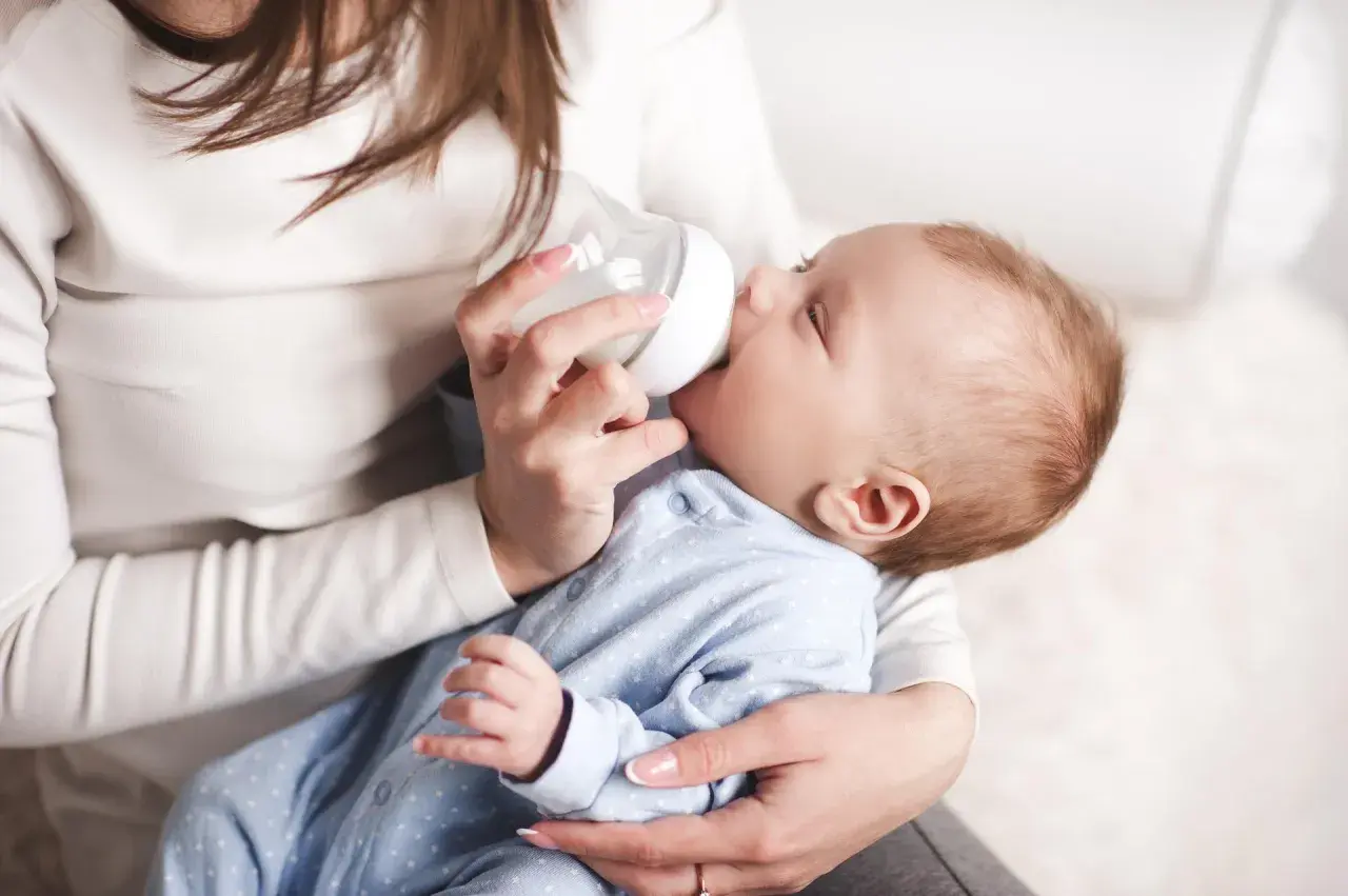 Delikatne karmienie noworodka butelką. Mama trzyma dziecko i podaje mu mleko, pokazując jak karmić noworodka butelką.