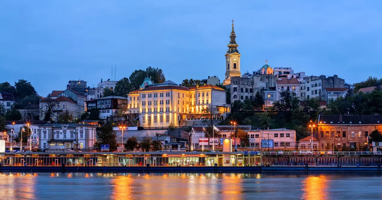 Wieczorny widok na wzgórze z budynkami i kościołem, odbijający się w rzece. Stolica Serbii, Belgrad, prezentuje się malowniczo.