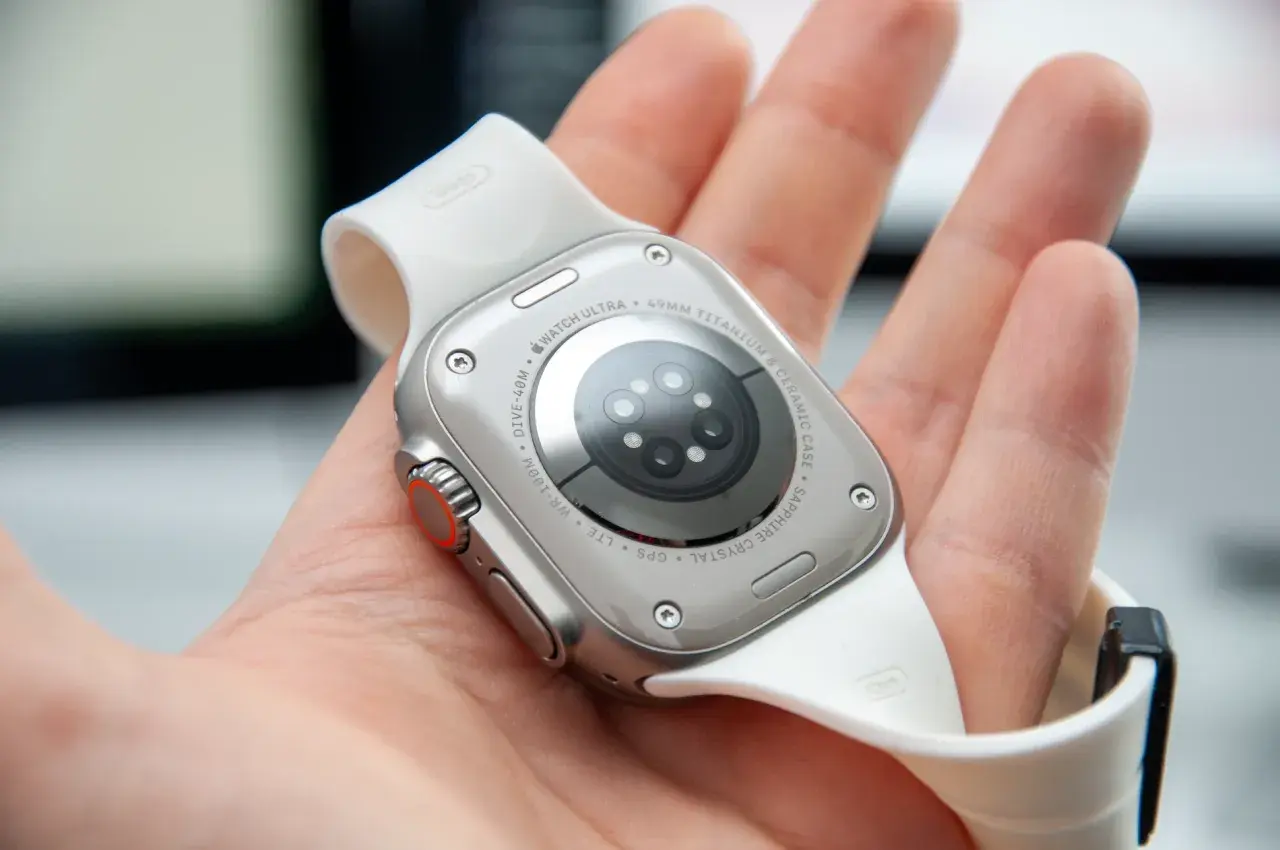 Naprawa smartwatcha Apple Watch Ultra. Widok na tył zegarka z białym paskiem, trzymanego w dłoni.