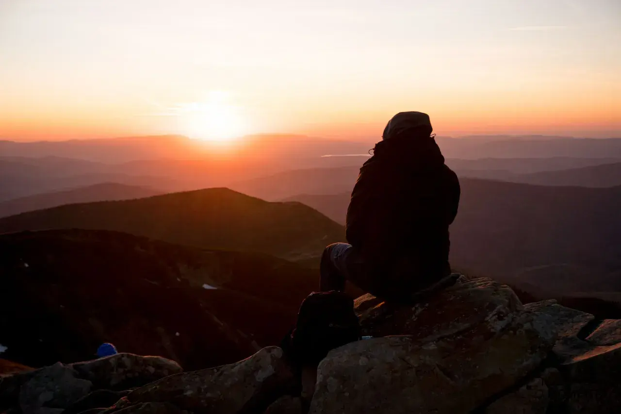 Sonnenuntergang in den Hohen Tatra. Eine Person sitzt auf einem Felsen und blickt auf die Berge.