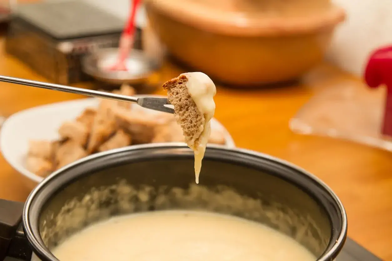 Un morceau de pain trempé dans une fondue savoyarde sans appareil. Le fromage dégouline sur la fourchette.