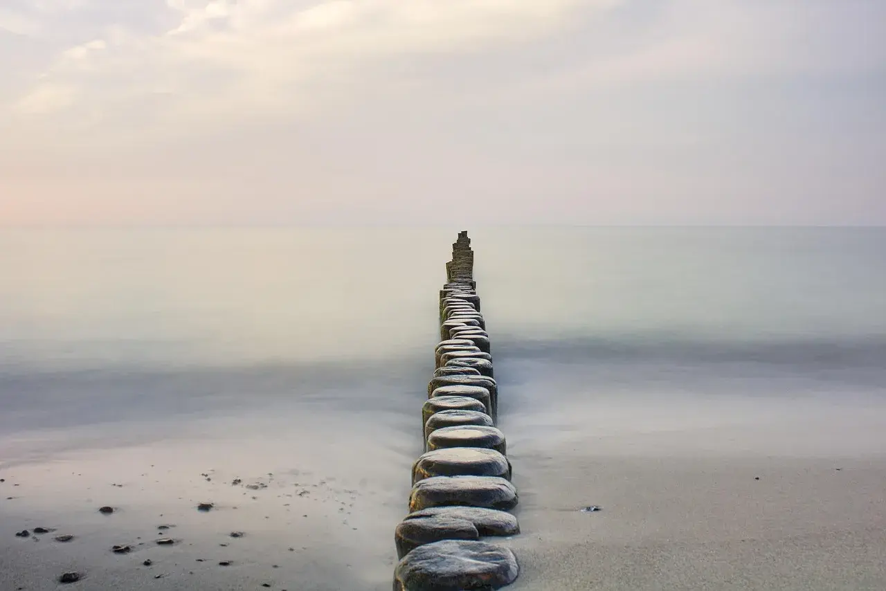 Linia drewnianych pali na plaży, prowadząca w spokojne morze, tworzy stan zen.