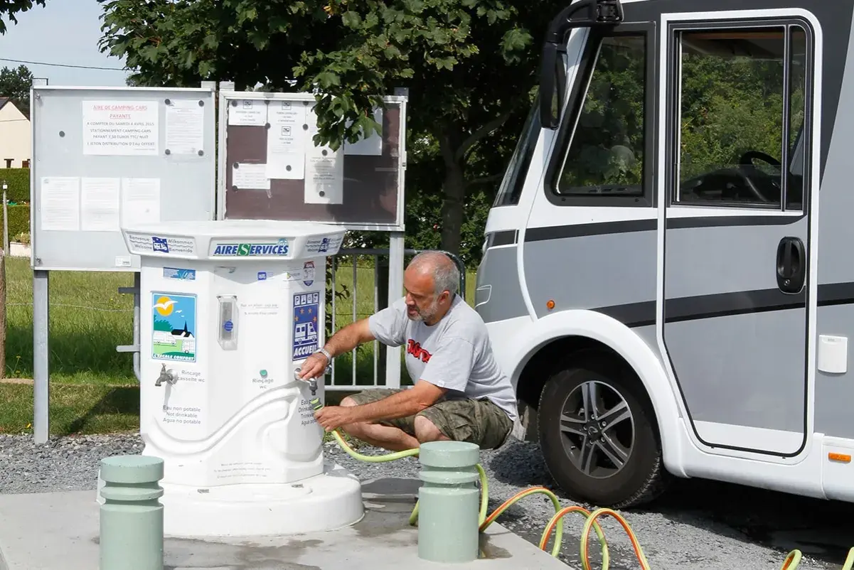 Un homme remplit un tuyau à un point d'eau pour camping-car. L'aire de services propose de l'eau potable et non potable.