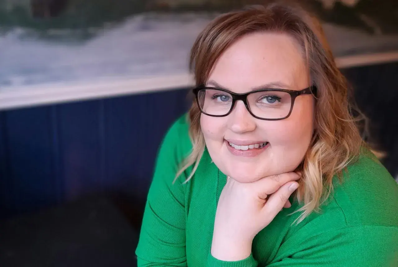Kvinna med glasögon och grön tröja ler, trots morgonens ångest och depression.