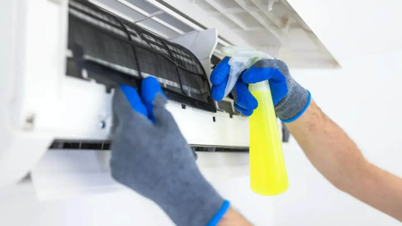 Manos enguantadas sacan filtro de aire acondicionado para limpiarlo con spray.