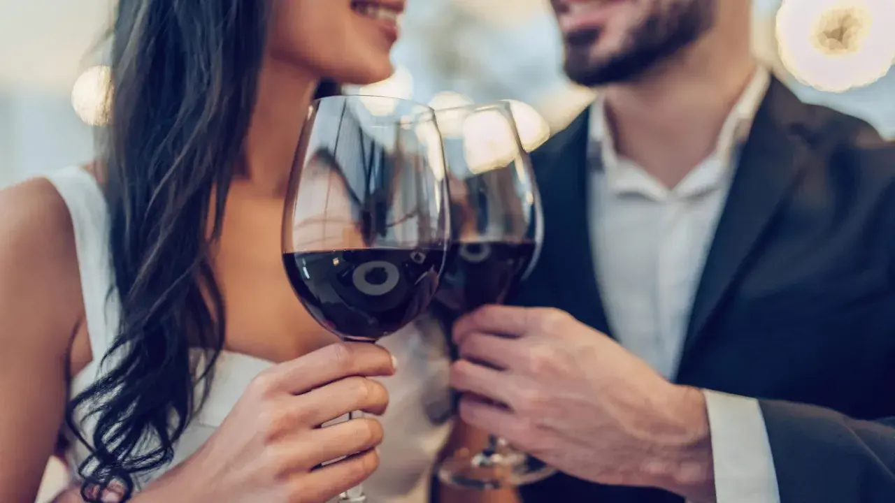 Ein Paar hebt Gläser mit Rotwein zum Anstoßen. Ein Glas Rotwein kann gesund sein, wenn er in Maßen genossen wird.