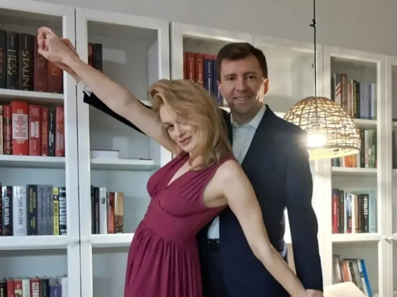 Łukasz Schreiber z żoną pozują na tle regałów z książkami. Ona w błyszczącej sukni, on w garniturze.