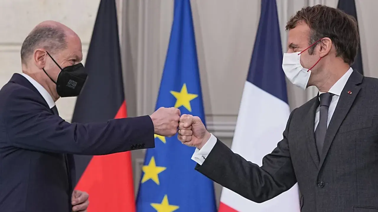 Olaf Scholz und Emmanuel Macron stoßen Fäuste vor den Flaggen von Deutschland und Frankreich.