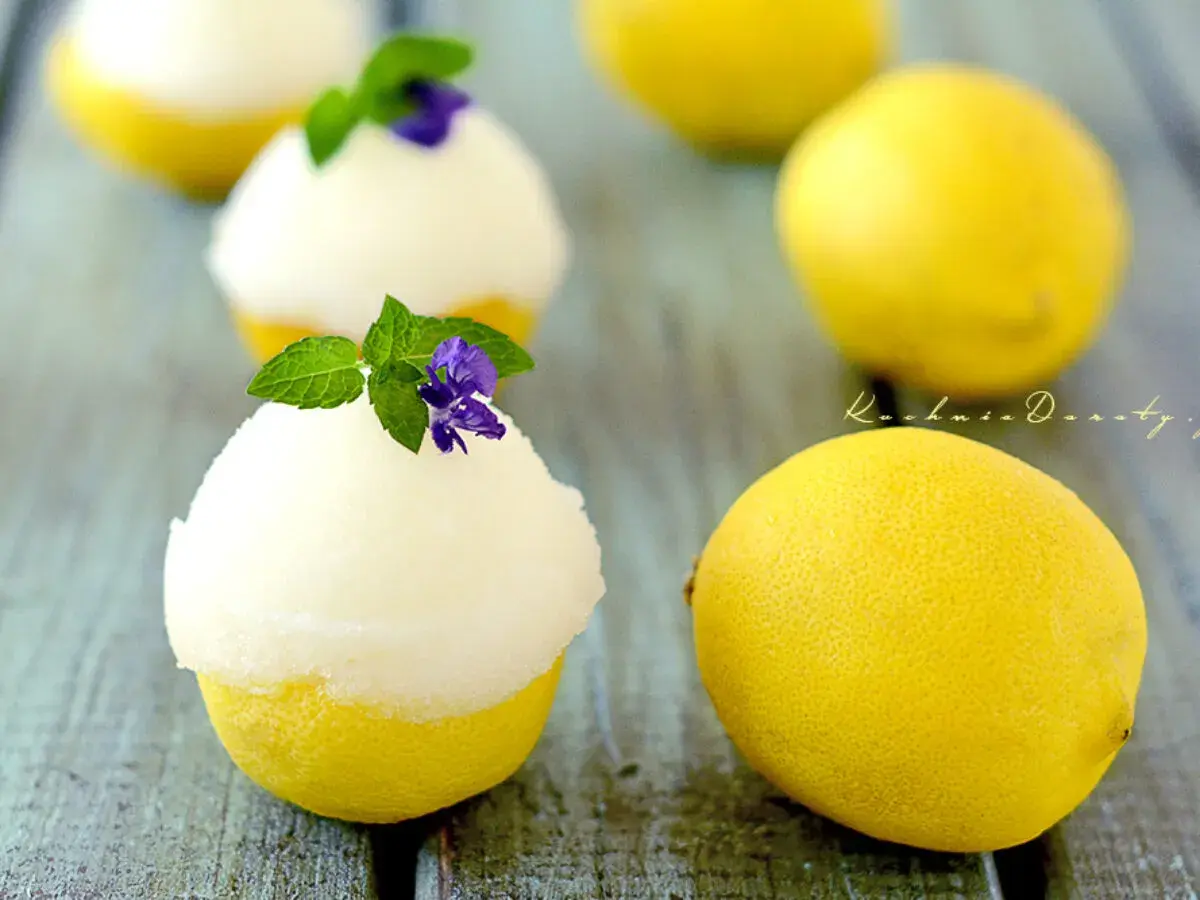 Orzeźwiający sorbet cytrynowy podany w wydrążonych cytrynach, udekorowany miętą i fioletowym kwiatkiem.