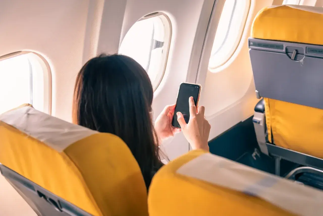 Kobieta w samolocie korzysta z telefonu, pamiętając o włączeniu trybu samolotowego.