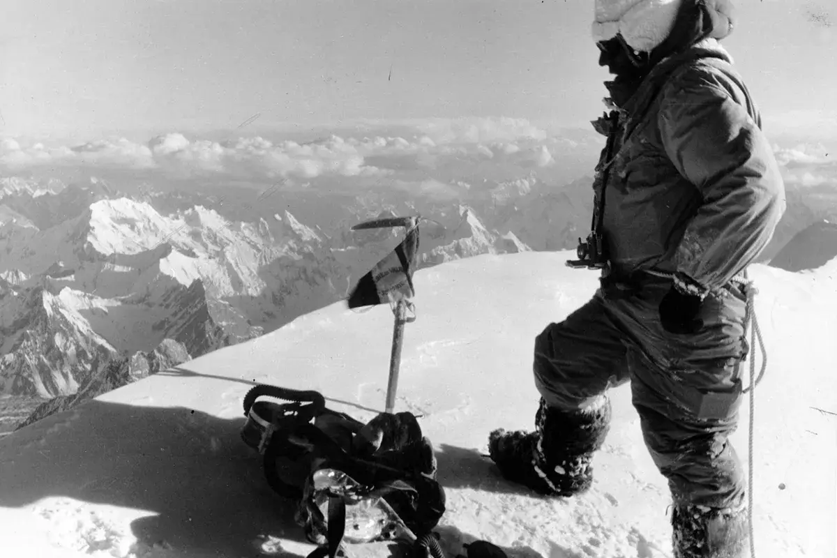 Bergsteiger auf dem Gipfel des K2, der die Erstbesteigung feiert. Ausrüstung und Fahne im Schnee.
