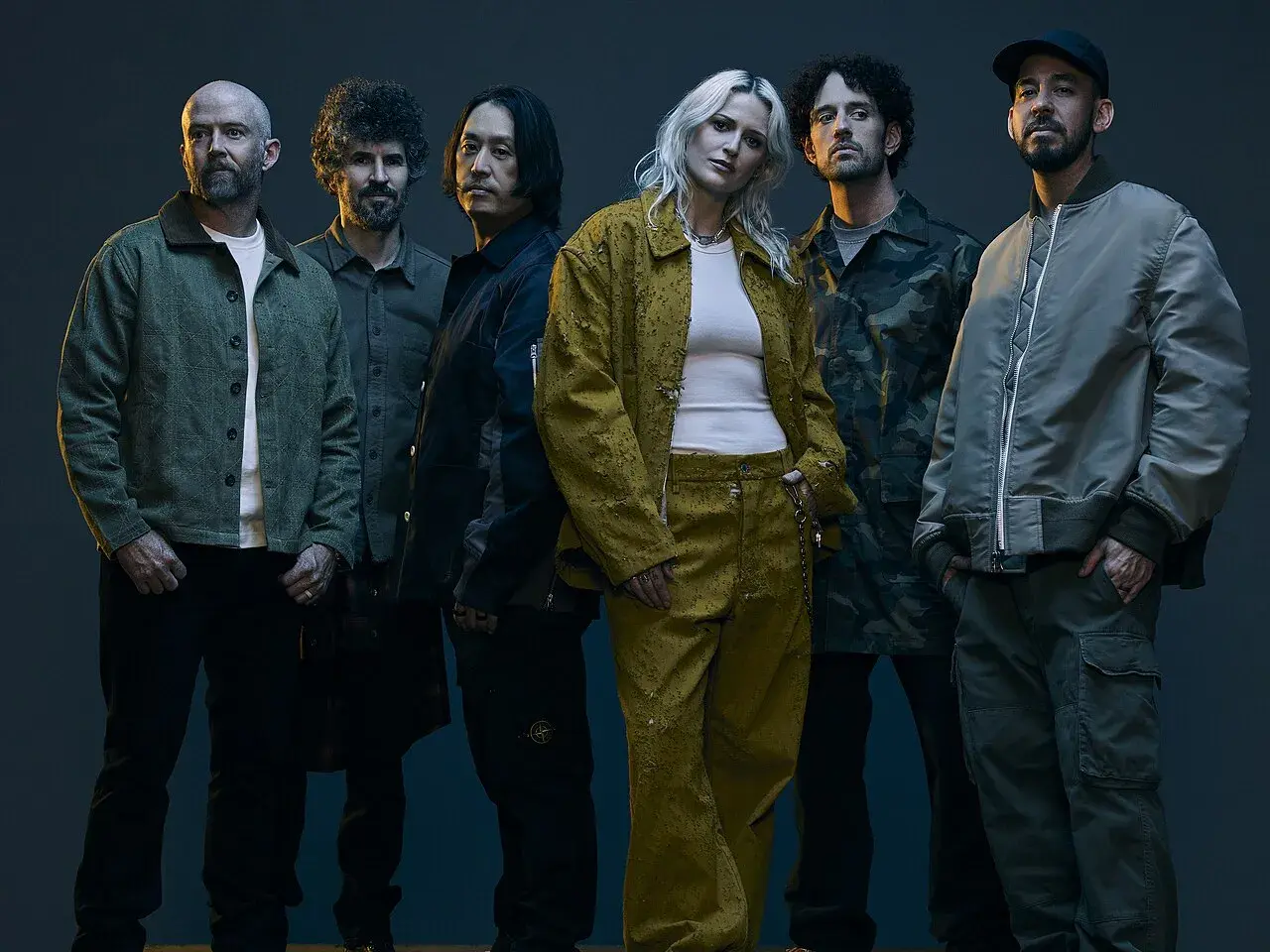 Sześcioro muzyków, w tym wokalistka w żółtym komplecie, pozuje do zdjęcia. Ich styl nawiązuje do **nu metal**owych klimatów.