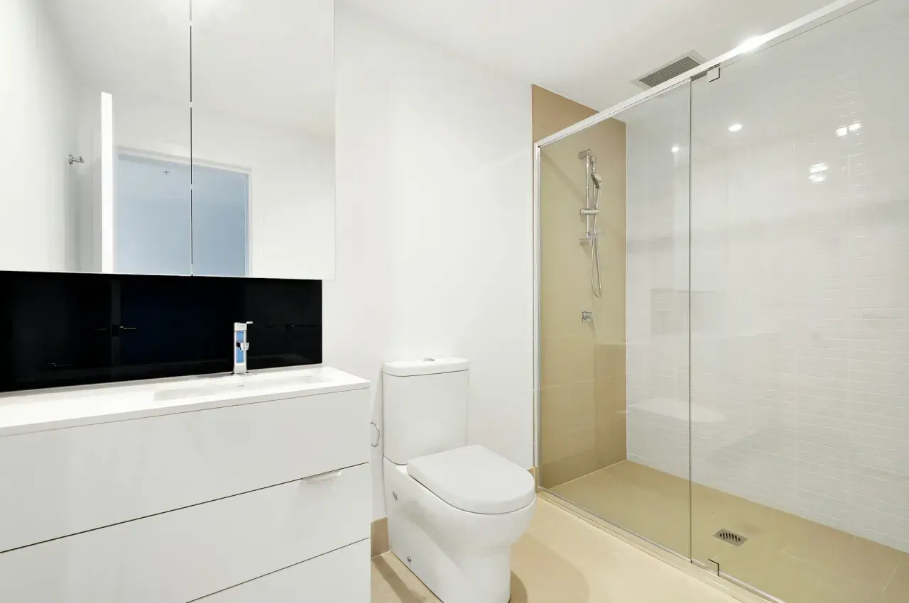 Mampara de ducha de cristal con medidas adecuadas para que no salga el agua. Baño moderno con lavabo, inodoro y ducha.