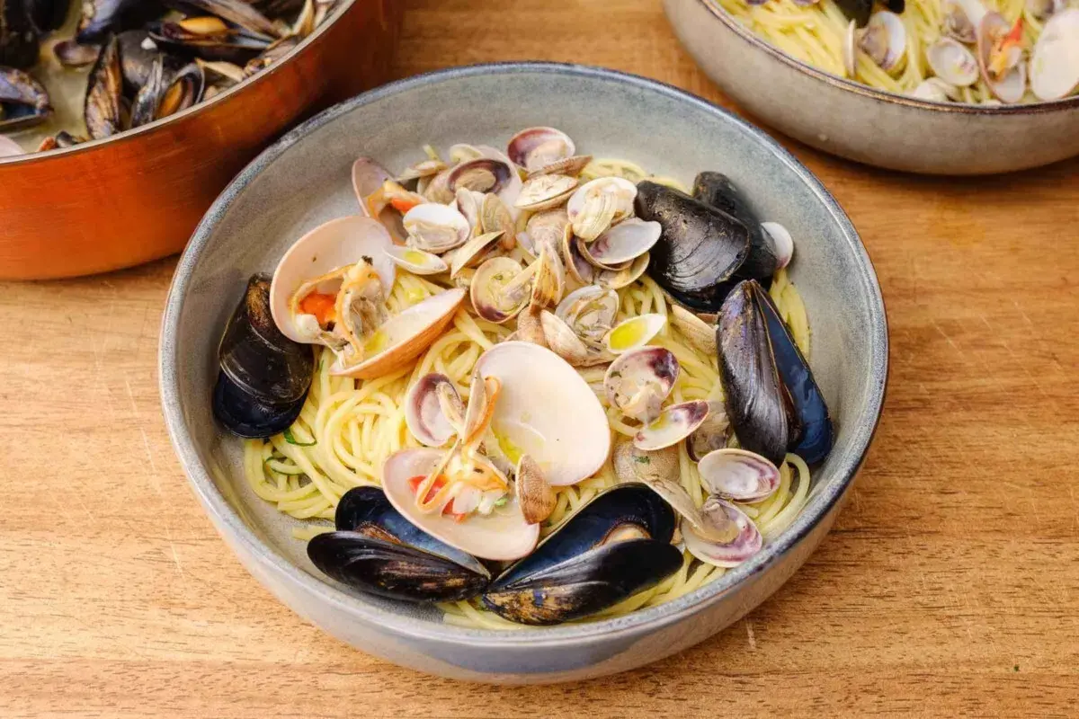 Spaghetti Vongole mit Muscheln und Venusmuscheln, serviert in einer Schüssel auf einem Holztisch.